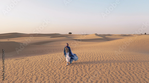Aerial view from a drone flying next to a woman in abaya United Arab Emirates traditional dress walking on the dunes in the desert of the Empty Quarter. Abu Dhabi, UAE.