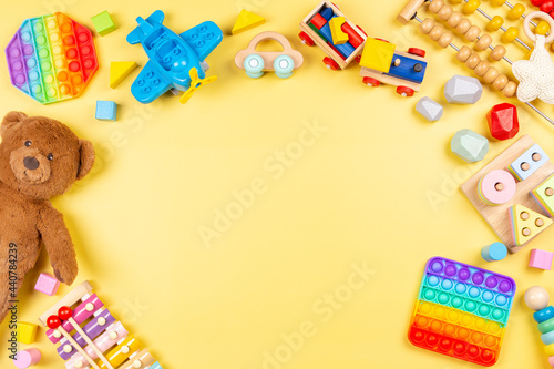 Baby kids toy background with teddy bear, wooden and musical toys, abacus, plane, pop it fidget toys and colorful blocks on yellow background. Top view, flat lay photo