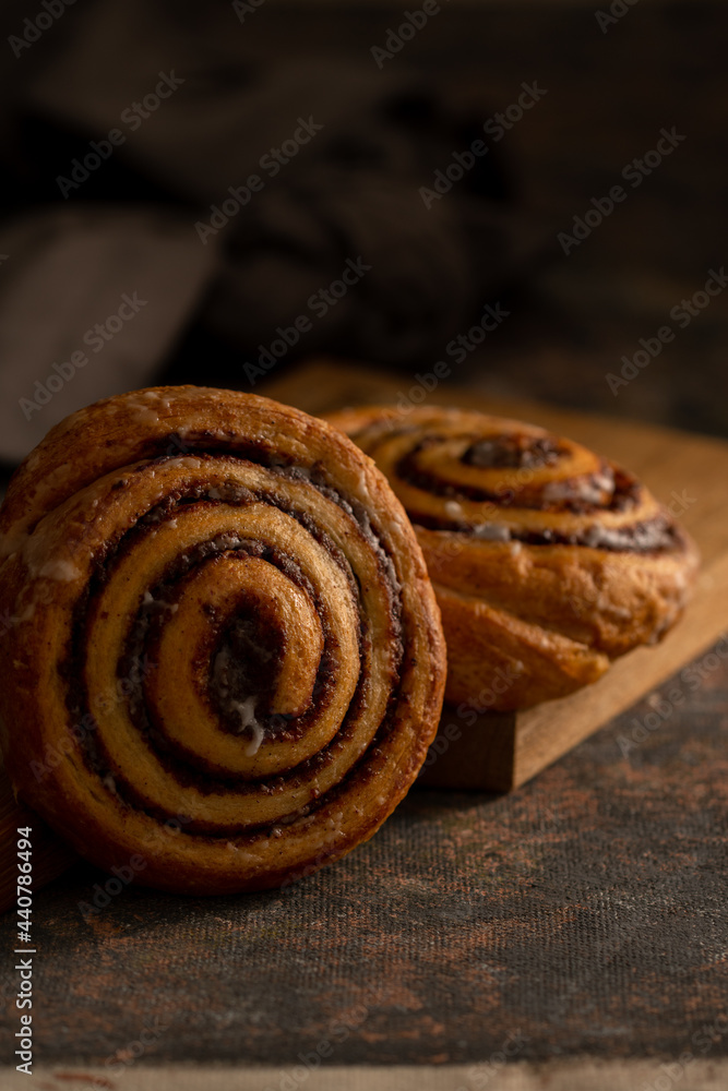 two cinnamon rolls on a wooden chopping board. Dark photo style. Dark background