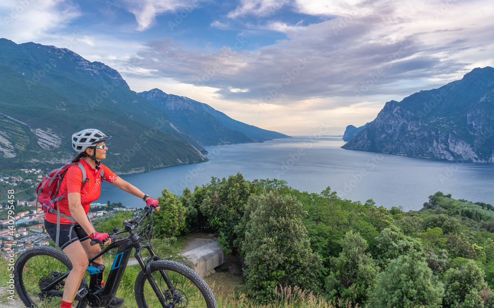 nice senior woman with elctric mountain bike resting on Monte Brione and enjoying the awesome view over Garda Lake between Riva del Garda and Torbole