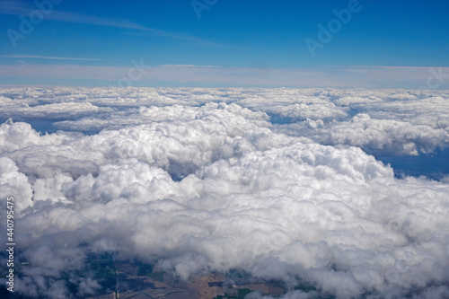 sky with thunderous white clouds above the ground view from the airplane window, horizontal.