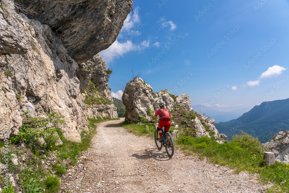 nice and active senior woman riding her electric mountainbike on the famous Tremalzo downhill from Tremalzo Pass to Riva del Garda at Garda lake, Trentino, Izaly