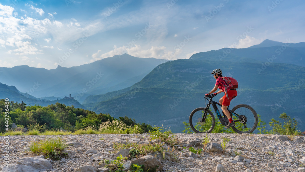 nice, active  senior woman riding her electric mountain bike in the huge rock fall area of Marocche di Dro, in the Sarca Valley, Garda lake mountains, Trentino, Italy 
