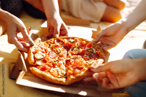 Fototapeta Naklejka Na Ścianę i Meble -  Hands taking slices of pizza close view. Group of Friends eating pizza at the beach. Fast food concept. Picnic at the beach. Summer vacation, holidays, travel, lifestyle  and people concept.