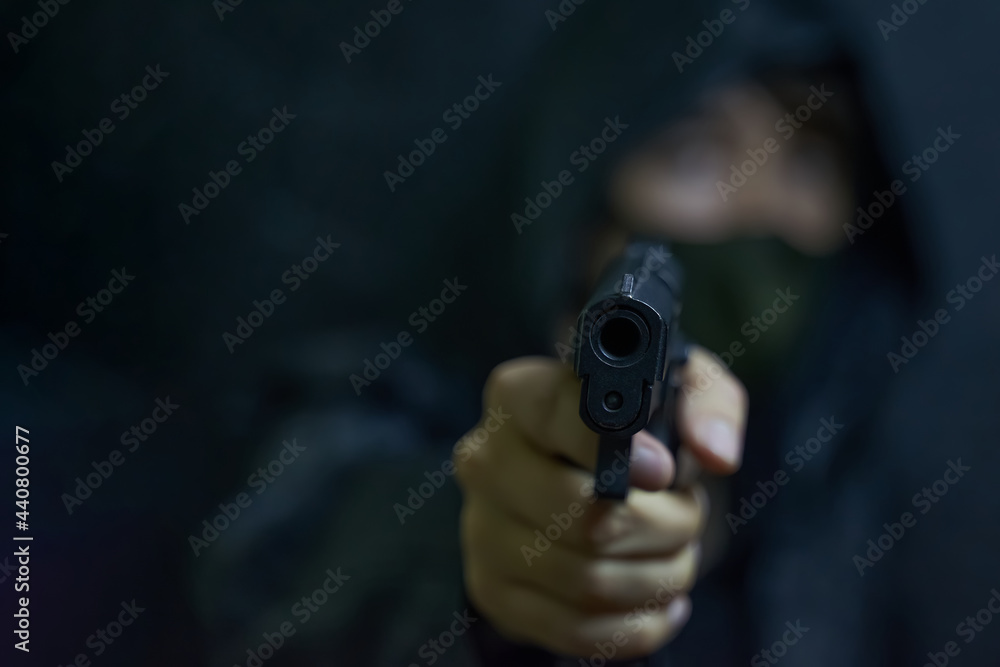 Man in hood and mask threatens with firearm. Revolver in person's hands. Murderer or armed thief. Criminal with a gun.