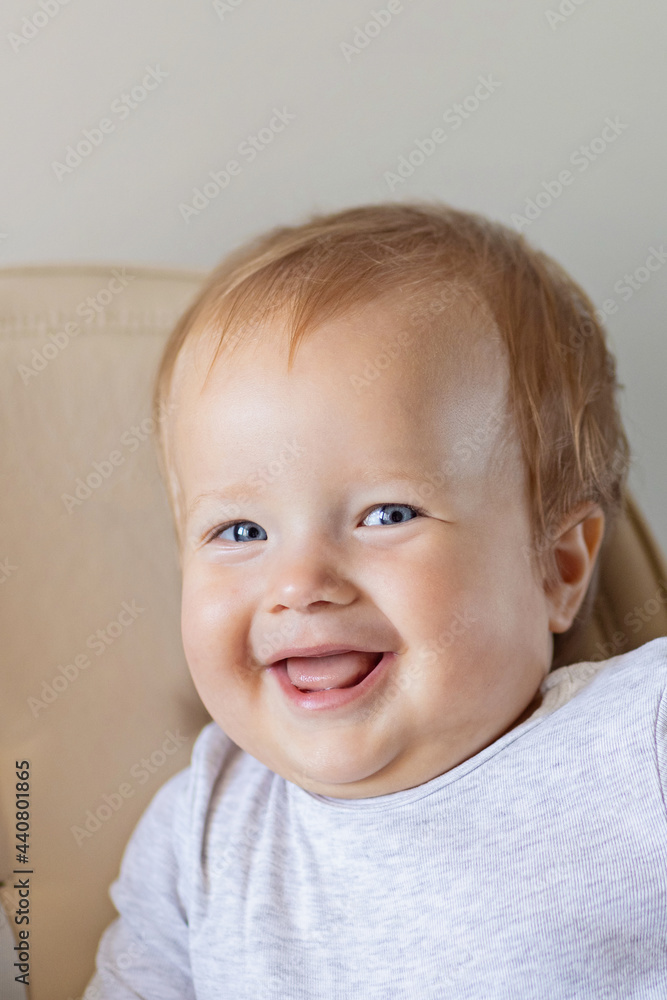 Cute caucasian infant girl ten months old sitting in baby chair and smiling on beige background. Closeup portrait of happy infant with blonde hair and blue eyes