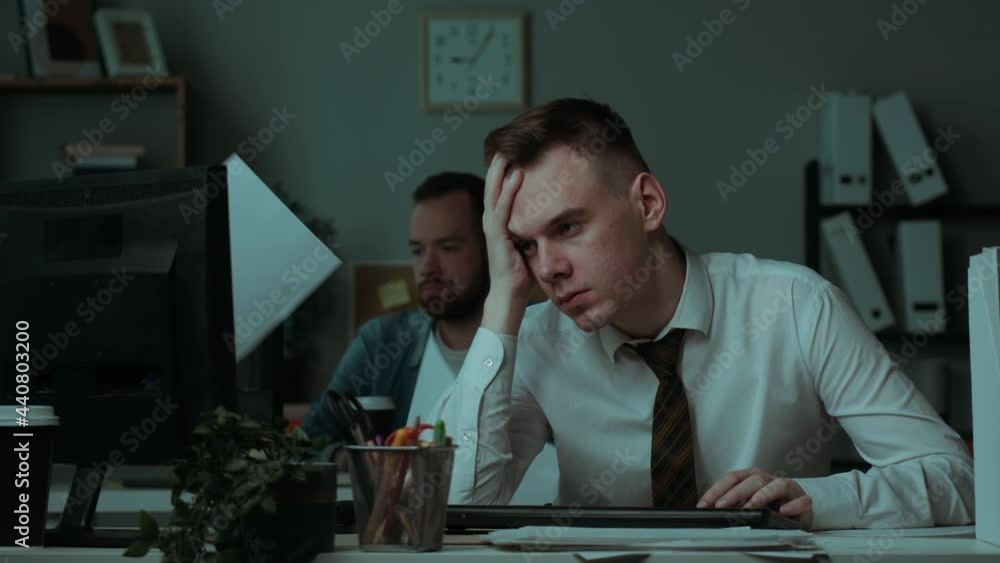 Tired irritated man working in office in evening, angry employee having headache, exhausted worker with red eyes, pain in head, executive business people working at night. Bad mood, fatigue at work. Tired irritated man working in office in evening, angry employee having headache, exhausted worker with red eyes, pain in head, executive business people working at night. Bad mood, fatigue at work.