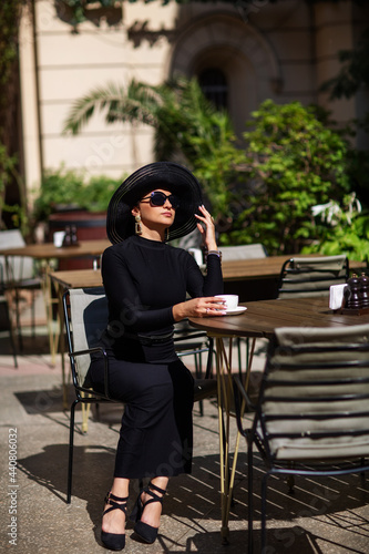 Canvas Print Exquisite woman in a black hat drinks coffee