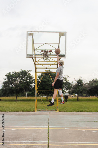 Young man making a jump shot for a basket ball on an abandoned basketball court.