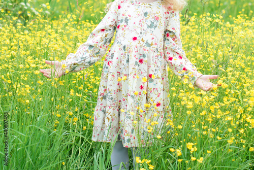 Little girl with in a summer dress stands in yellow flowers. Child in a flower meadow with yellow flowers.
