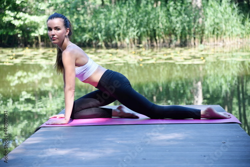 Woman in her 30's practicing yoga and meditation. Fit woman on wooden platform at the pond, surrounded by trees and water.