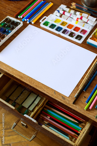 Artist's table with a blank sheet of paper and art tools, selective focus