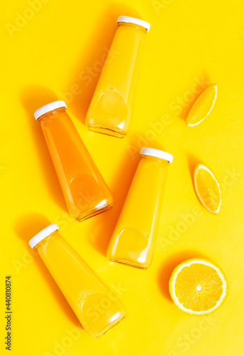 Bottled orange juice and oranges on a yellow background. The concept of a juicy, bright summer