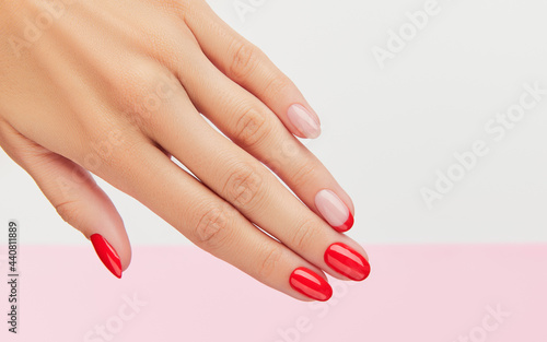 Womans hand with fashionable red manicure over white and pink background
