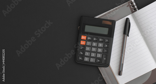 Calculator, notebook, pen on black leather background. Top view with copy space. Flat lay composition.