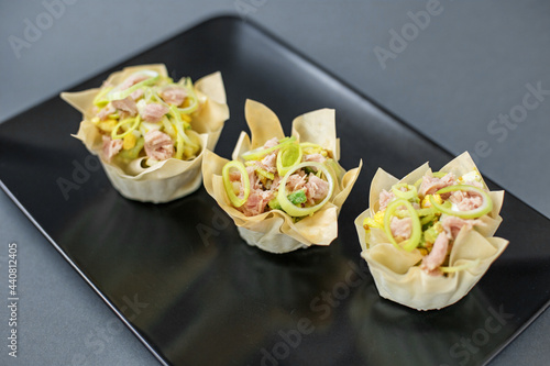 Three tartlets with tuna and onions on a black plate, buffet appetizer for buffets. Beautifully decorated catering banquet menu. Food snacks and appetizers for buffet.