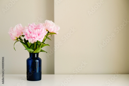 Studio shot of beautiful peony flowers in blue glass vase on a table over gray wall background with a lot of copy space for text. Feminine floral composition. Close up  backdrop.