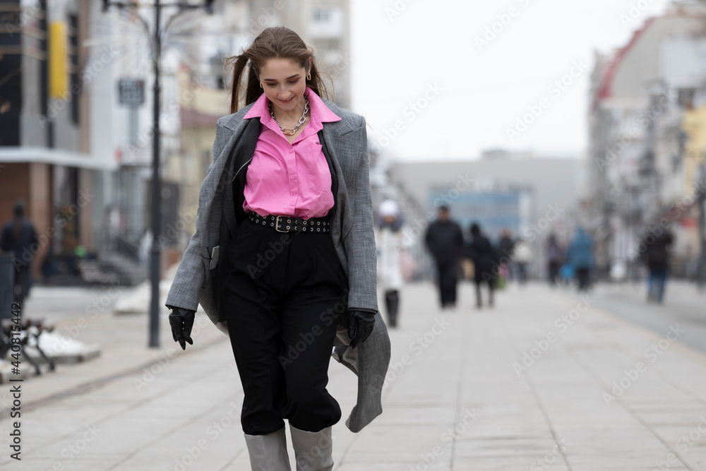 Young fashionably dressed and shy girl teenager 22 years old walks along the avenue or street with her head down and looking at her feet in the city on a blurred background of a crowd of people Young fashionably dressed and shy girl teenager 22 years old walks along the avenue or street with her head down and looking at her feet in the city on a blurred background of a crowd of people