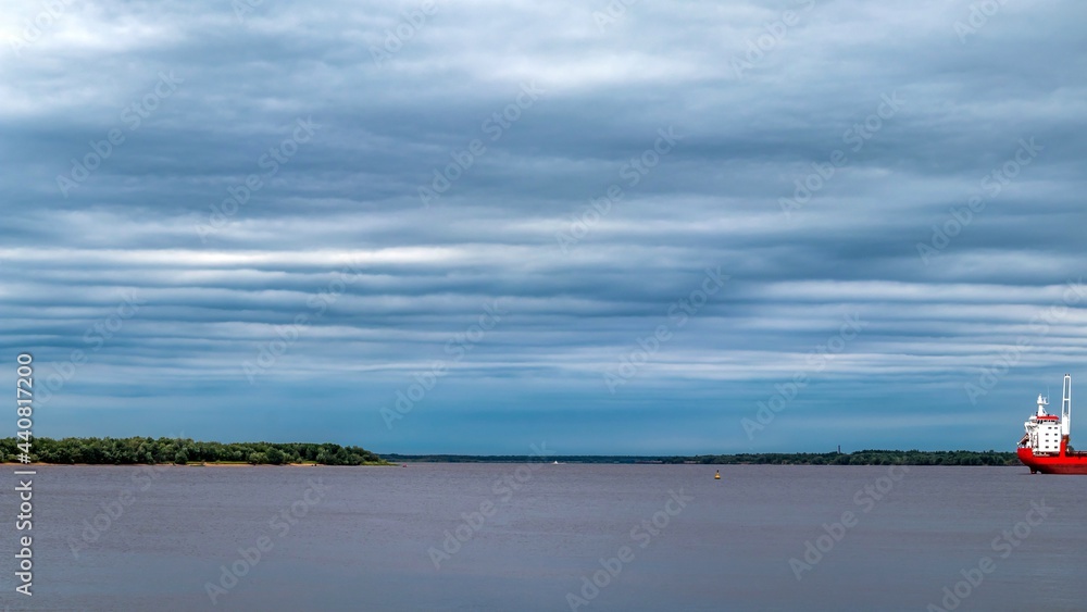 Cloudy sky above the water surface of a large river. Marine vessel in the roads. Northern Dvina, Arkhangelsk, Russia