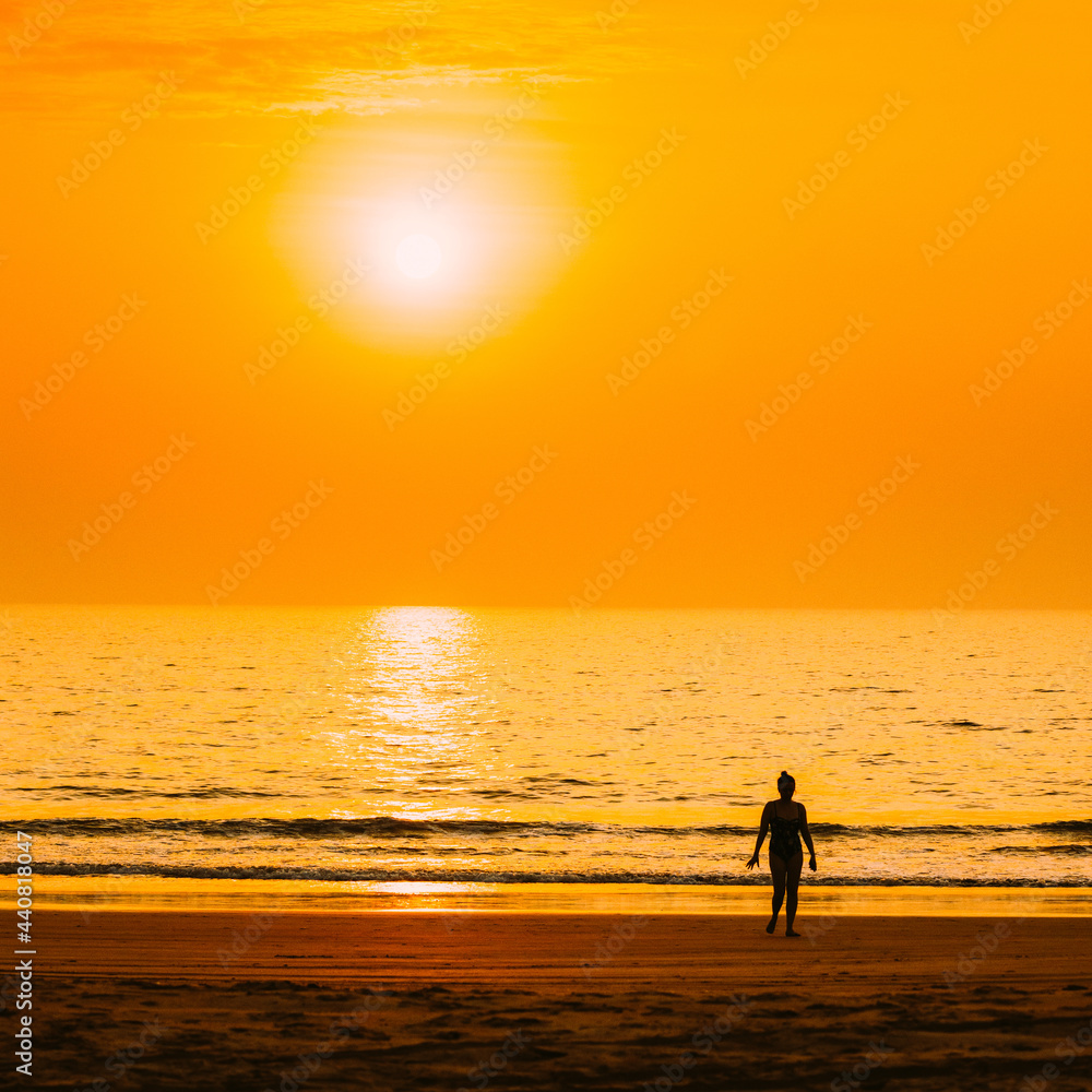 Silhouette Of Young Caucasian Lady Woman In Swimsuit Walking In Sea Beach During Sunset. Vacation On Ocean Beach. Sundown Above Sea Horizon At Sunset. Natural Sunrise Sky Warm Colors Over Ocean