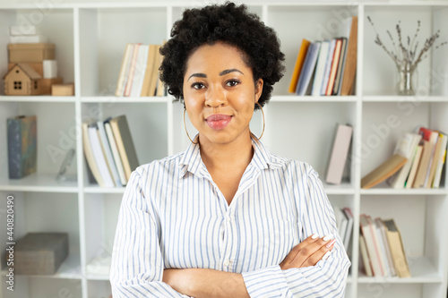 Portrait of a happy African American woman in the interior. Black smiling female student on the background of shelves with books.