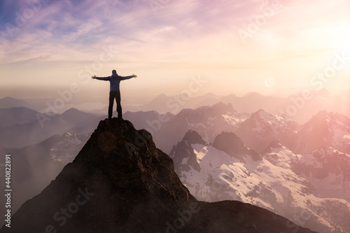 Adventure Composite. Adventurous Man with Open Hands is hiking on top of a mountain. Colorful Sunset or Sunrise Sky. 3D Rocky Peak. Aerial Background Landscape from British Columbia  Canada.