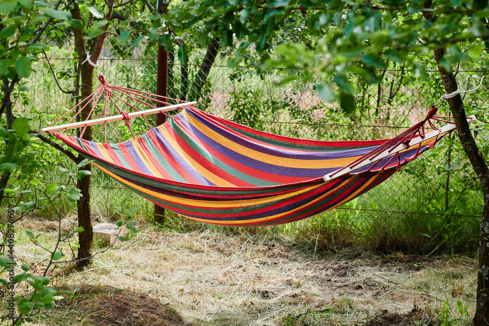 Colored striped hammock hanging on the lawn in the trees, a place for relaxation and rest