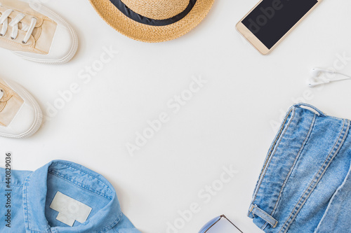 Flat lay summer composition with a straw hat, jeans and sneakers on a white background