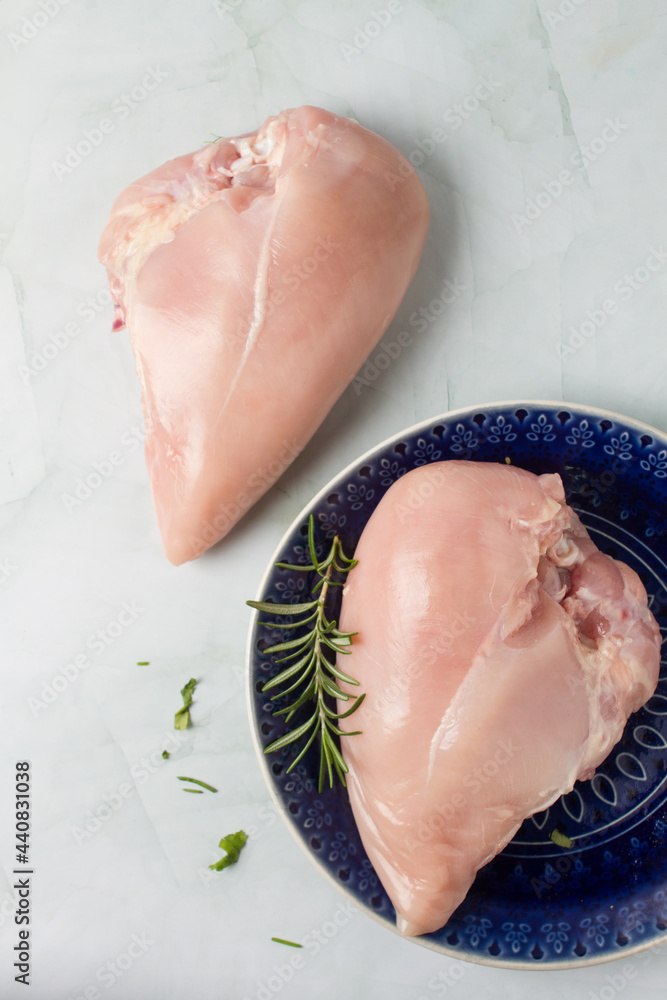 Raw chicken breast without skin, with herbs in a blue plate, green