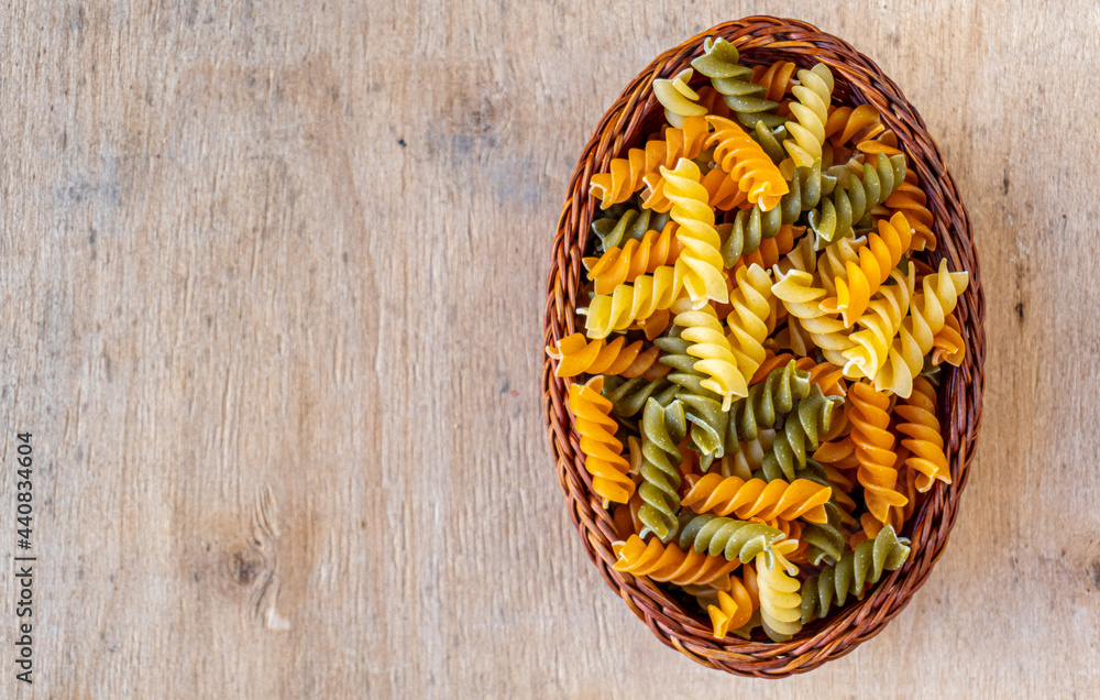 Raw and dry colored pasta in a spiral shape, on a wooden background.