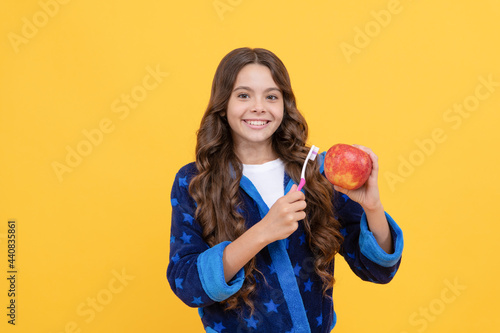 happy child girl in cozy bathrobe use toothbrush and hold apple, health