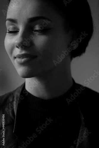 A happy young girl in a black leather jacket and short hair is sitting at a table. Black and white portrait of a smiling woman	