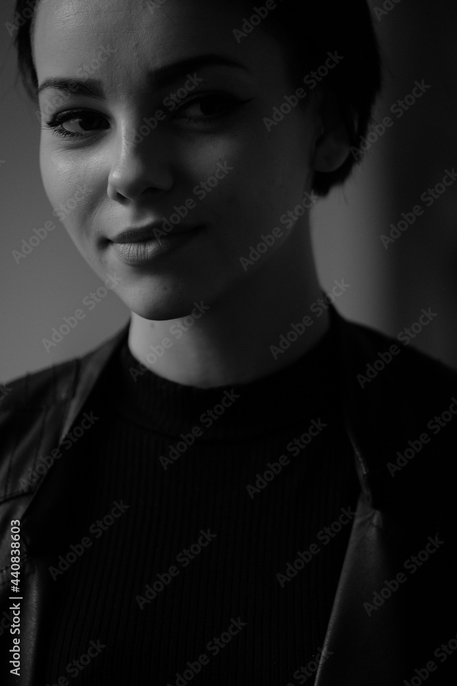 A happy young girl in a black leather jacket and short hair is sitting at a table. Black and white portrait of a smiling woman A happy young girl in a black leather jacket and short hair is sitting at a table. Black and white portrait of a smiling woman