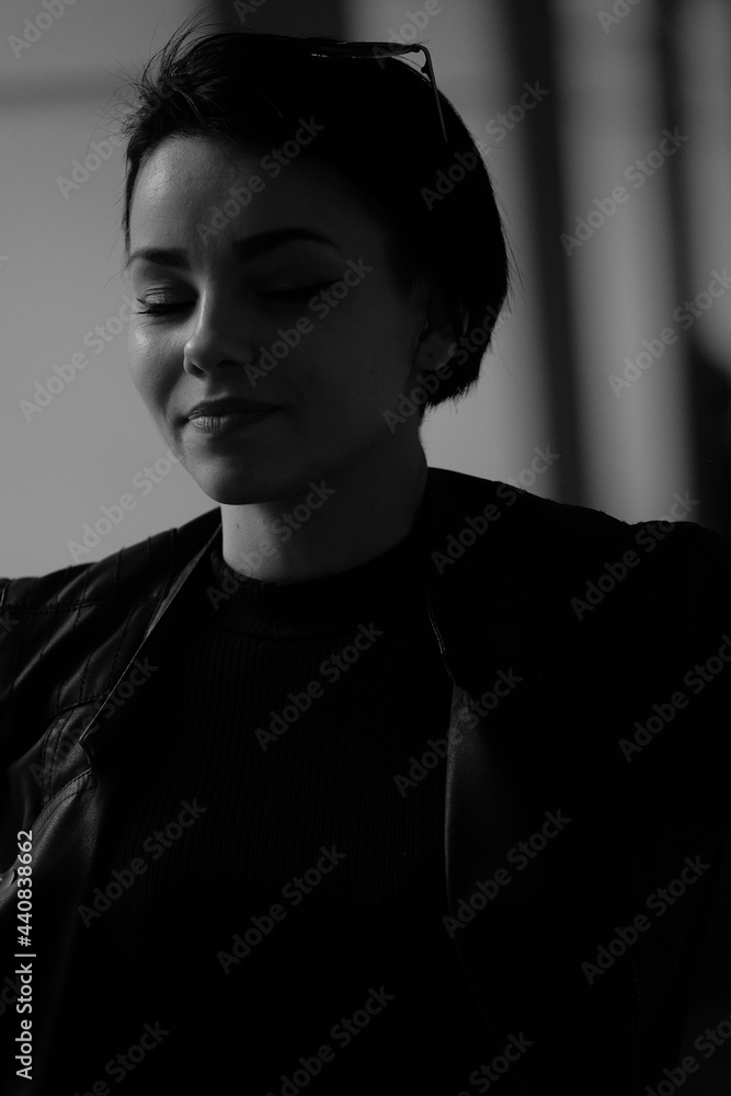 A happy young girl in a black leather jacket and short hair is sitting at a table. Black and white portrait of a smiling woman A happy young girl in a black leather jacket and short hair is sitting at a table. Black and white portrait of a smiling woman