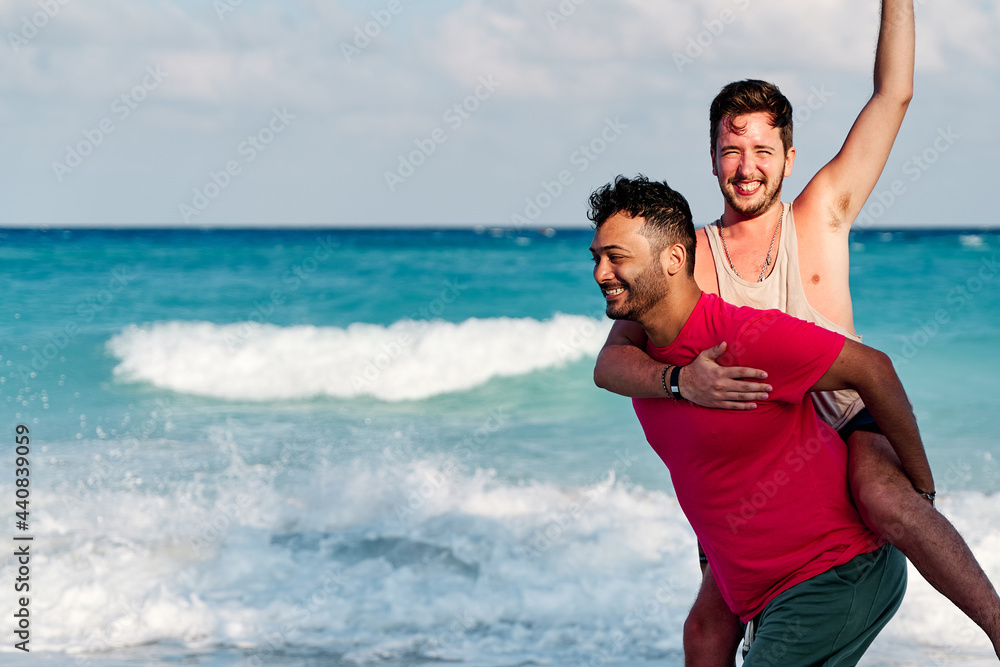 homosexual couple of two men playing piggybacking on the shore of cancun beach