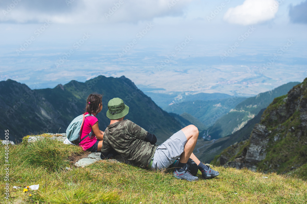 Father with his little girl resting on a mountain top and admiring the landscape