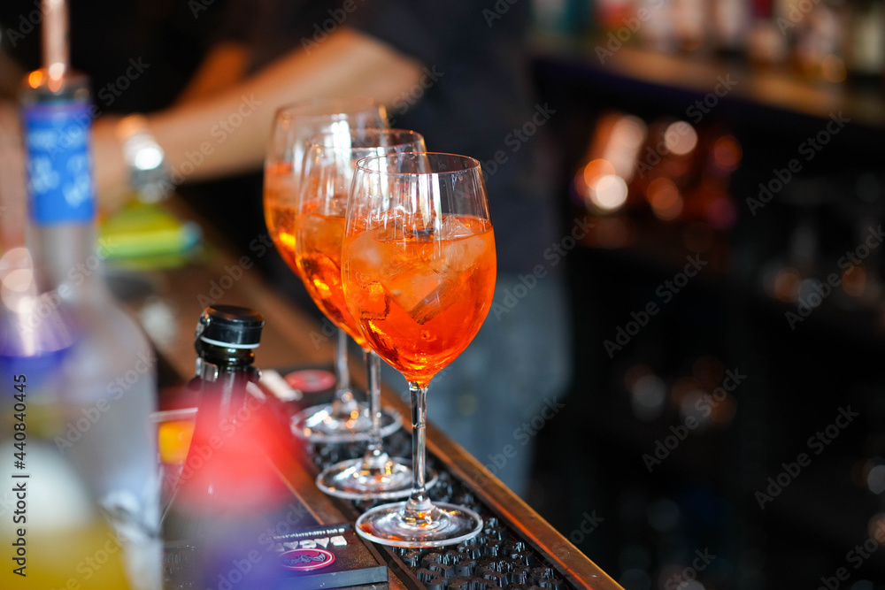 three glasses of cocktails on the bar. bartender pours a glass of sparkling wine with Aperol.