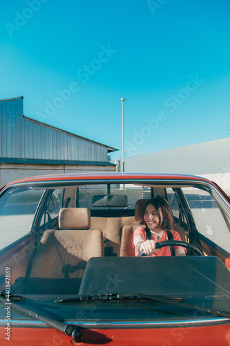 Woman in car indoor keeps wheel and turning around while smiling looking at the window