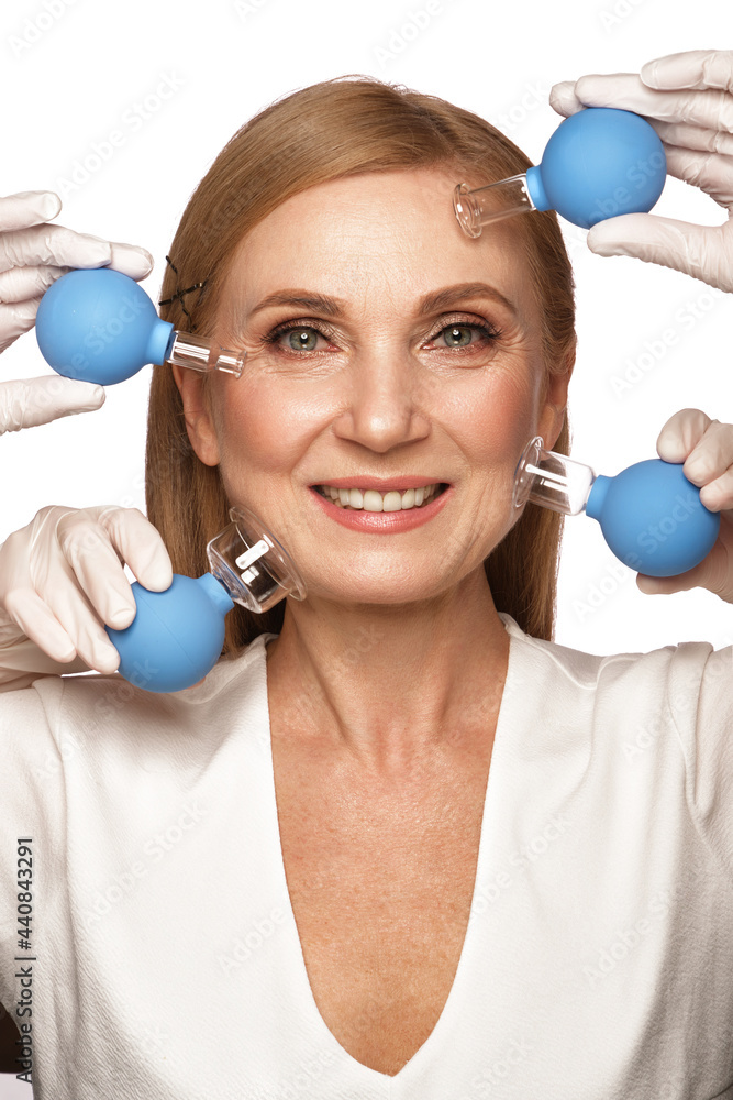 Portrait of a beautiful elderly woman in a white shirt with classic makeup and blond hair with massage tools in hands Portrait of a beautiful elderly woman in a white shirt with classic makeup and blond hair with massage tools in hands