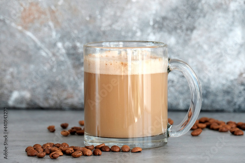 Cappuccino in a glass transparent large glass next to the coffee beans. Gray background.