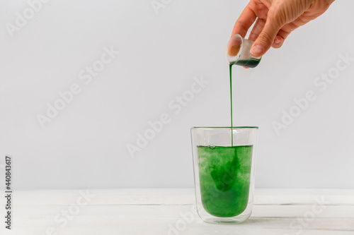 Woman hand pouring liquid chlorophyll in a glass cup. White background photo