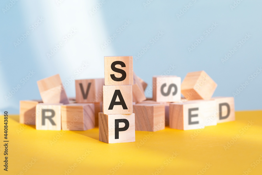 Obraz premium wooden cubes with letters sap arranged in a vertical pyramid, yellow background, reflection from the surface of the table, business concept