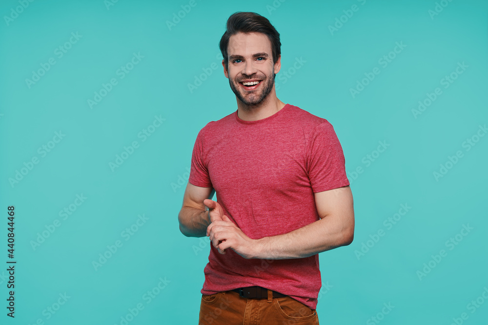 Handsome young man in casual clothing looking at camera and smiling while standing against blue background Handsome young man in casual clothing looking at camera and smiling while standing against blue background