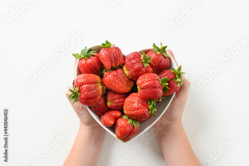 Tasty dessert of organic homegrown strawberry in child hands in plate shaped of heart on white background. Concept organic products.