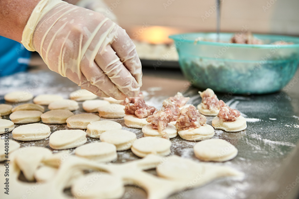 Chef hands sculpt dumplings on background of cutting boards with handmade, ravioli and khinkali sprinkled with flour on a table. Delicious homemade food.