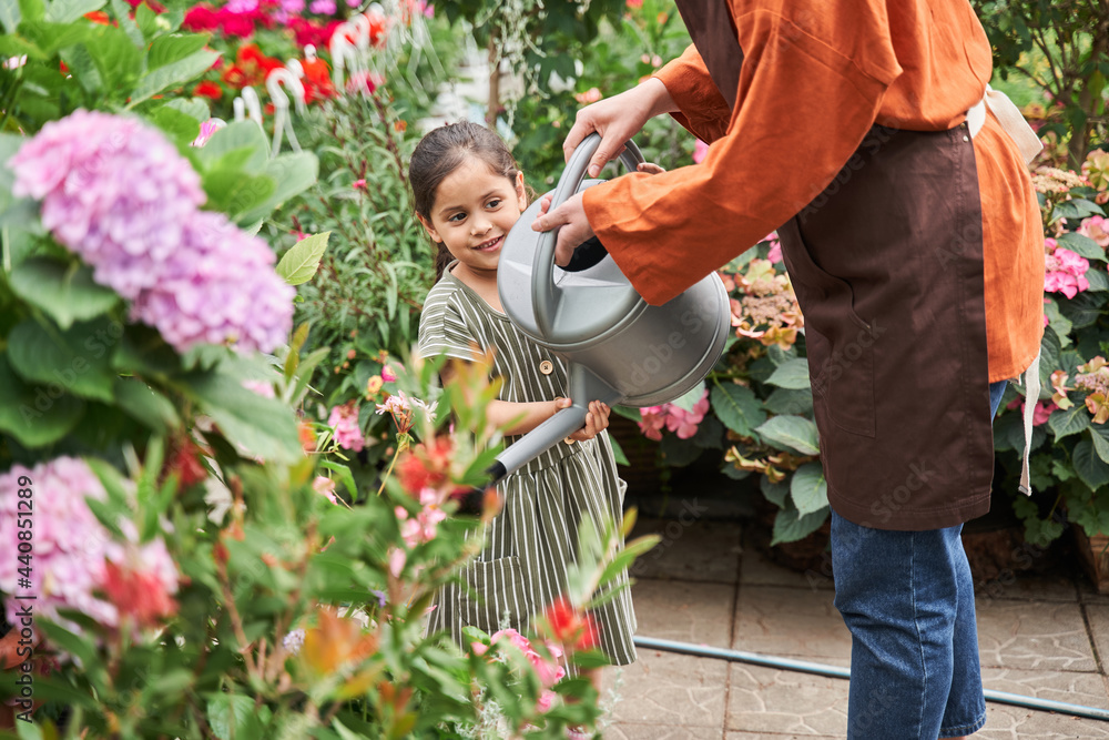 Fototapeta premium Girl helping to her senior grandmother while holding a watering can over bushes