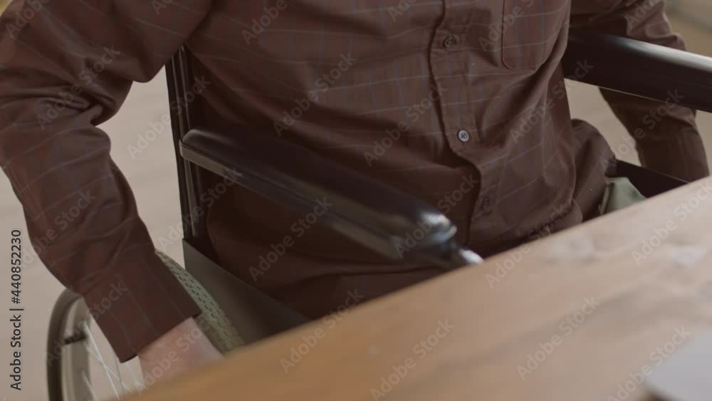 Slowmo close-up of unrecognizable elderly man in wheelchair working on laptop in modern office Slowmo close-up of unrecognizable elderly man in wheelchair working on laptop in modern office