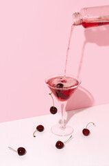 Pouring sparkling cherry beverage into a cocktail glass on pink background