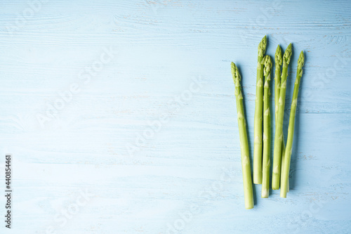 Fresh green asparagus on blue wooden background, place for text. Flat lay.