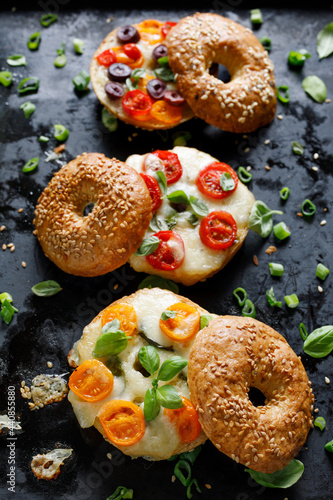 Grilled bagel sandwiches with with cherry tomatoes, olives, mozzarella cheese and herbs  on a dark background, focus on the sandwich with yellow tomatoes, close up